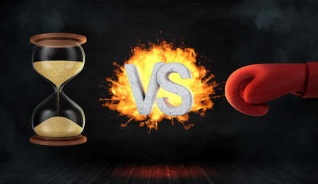 3d rendering of a concrete letters VS caught on fire between an hourglass and a red boxing glove.の写真素材