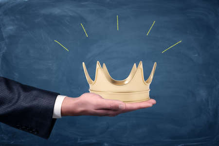 A male businessmans hand holding a golden crown on an open palm. Invitation to fist class.の写真素材