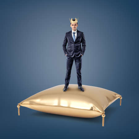 An assured businessman wearing a golden crown stands on a golden cushion.の写真素材