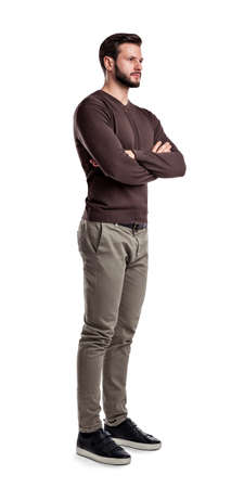 A young man in jumper and cargo pants stands looking in front in half-turned view with arms folded on his chest.の写真素材