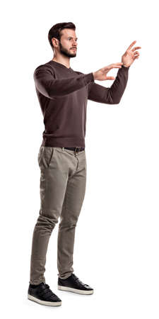 A young man in fashionable casual closes stands on a white background with hands as if pressing invisible buttons.の写真素材