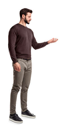A young man in fashionable casual closes stands in a side view and looks at one hand turned up as if holding something.の写真素材