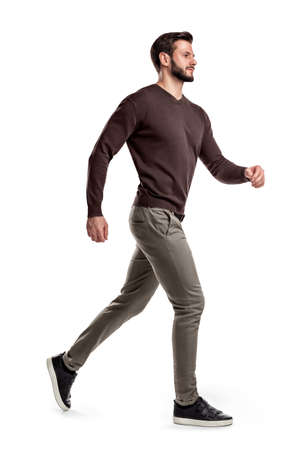 A young bearded man in a side view walks fast on the verge of running on a white background.の写真素材