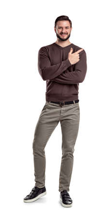 A bearded man in casual clothes keeps one leg bent white smiling and showing direction with one of crossed hands.の写真素材