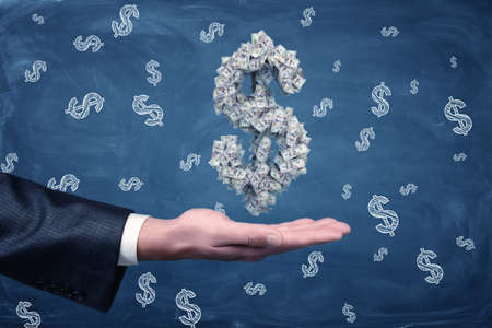 A male businessmans hand holding a large dollar sign made of banknotes at hand.