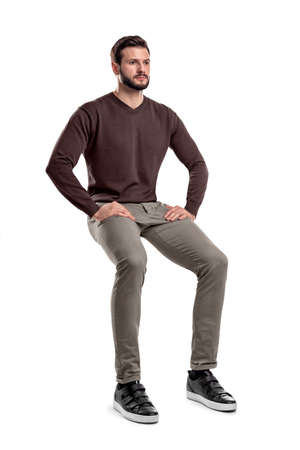An isolated bearded man in casual wear sits on a white background with hands on his thighs.の写真素材
