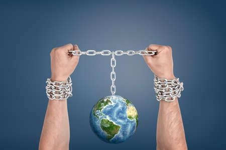 Two male hands bound together with chains and linked to an Earth globe between them.の写真素材