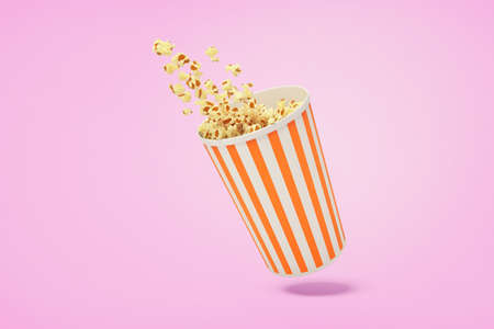A traditional striped carton can full of pop-corn with some kernels flying out on a pink background.の写真素材