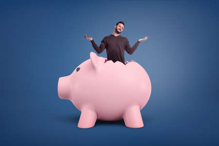 A small bearded man with a confused appearance sticks out from a crack in a giant pink piggy bank.の写真素材
