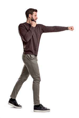 An isolated bearded man in casual clothes stands in a side view and punches empty air with one arm.の写真素材