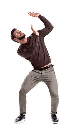 A bearded man in casual garb stands protecting himself with outstretched hands from something getting to him from above.