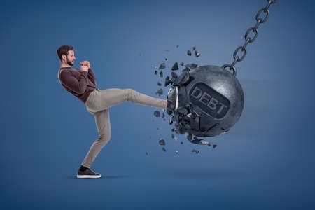 A man in casual clothes kicks a giant wrecking ball with a word DEBT written on it.の写真素材
