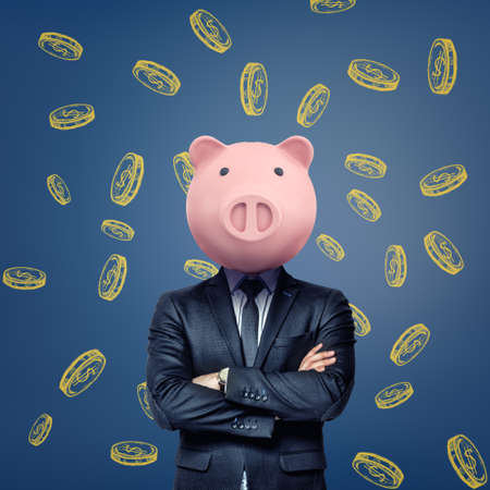 A businessman with folded arms stands wearing a pink pig mask on a background with chalk golden coins.の写真素材