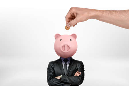 Hand inserting coin into piggy bank head of a businessman on white backgroundの写真素材