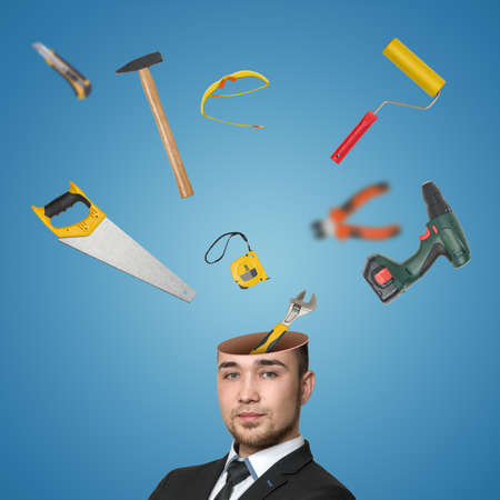 A view of a handsome young mans head cracked open with various tools popping out isolated on blue background.の写真素材
