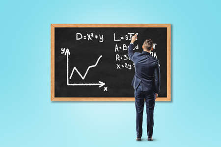Businessman writing formula on chalkboard or blackboard on blue backgroundの写真素材