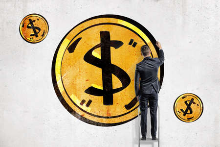 A back view on a businessman finishing drawing a yellow dollar coin on a white wall.