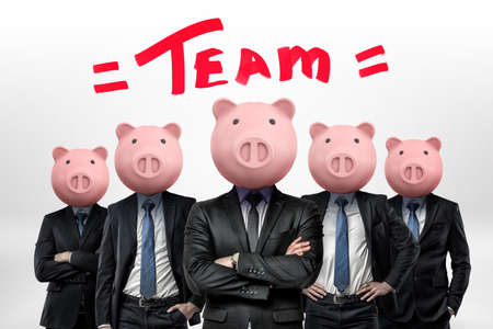Several businessmen with piggy bank heads stand close to each other under the word Team.の写真素材