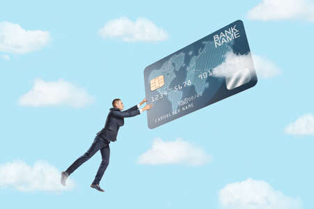 A small businessman flies in the sky and grabs a giant credit card in a jump. Living for money.の写真素材