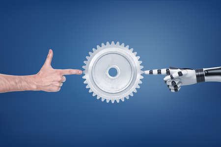 A large metal spur gear with a human and a robotic hand touching it from different sides.の写真素材