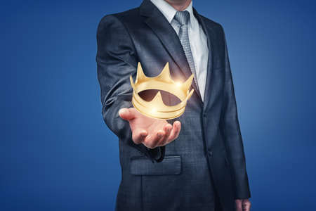 A bright golden crown hangs right above a businessmans hand and sparkles.の写真素材