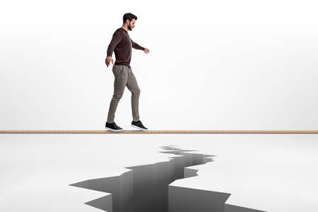 A bearded man is very concentrated when walking on a tight rope above a crack in the earth.の写真素材