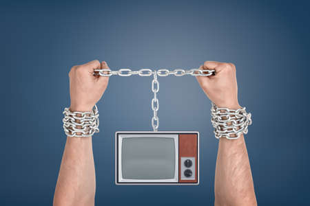 Two male hands bound together with metal chains and linked to a retro TV unit with blank screen.