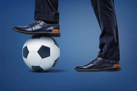 Giant businessmen legs with one foot standing on a soccer ball holding it in place.の写真素材