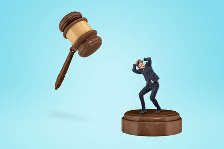 Tiny businessman about to be smashed by an inscribed gavel.