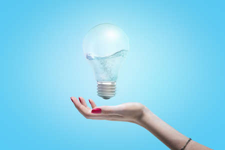 Womans hand with open palm as if about to take hold of an electric bulb floating in the air with water inside the bulb.の写真素材