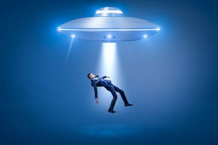 A businessman pulled toward an open hatch of a UFO by some invisible force.の写真素材