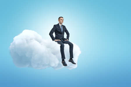 A young businessman sitting on a white fluffy cloud in the blue sky with lots of copy space left.の写真素材