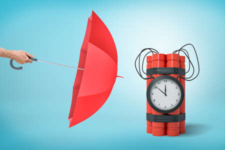 Male hand with red umbrella pointing to red dynamite time bomb on blue backgroundの写真素材