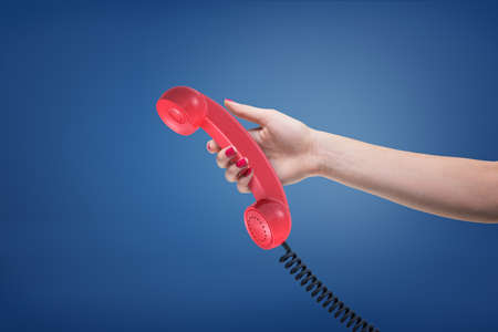 A female hand with painted nails holds a red retro phone receiver with a black cord.の写真素材
