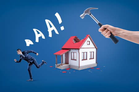 A hand holding a hammer breaking small houses roof with a businessman running away screaming.