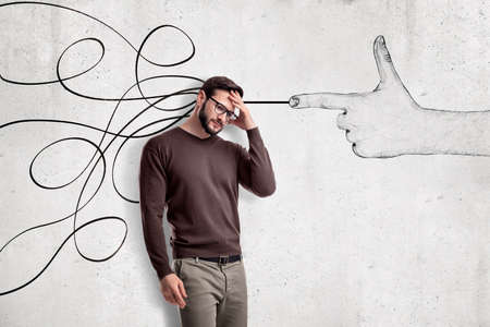 Thinking young man in casual clothes with a hand shooting gesture and abstract lines drawn on white wall backgroundの写真素材