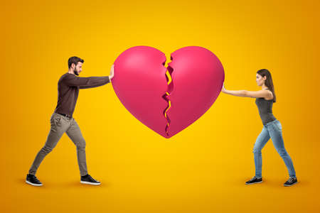 Young man and woman wearing casual clothes holding pink broken heart together on yellow background