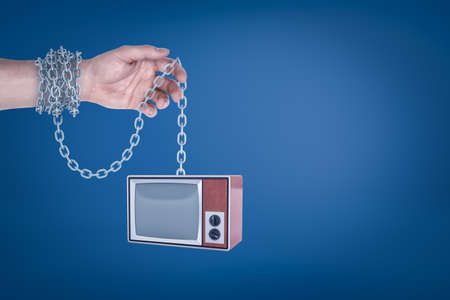 Close-up of mans hand with metal chain around wrist holding retro TV set hanging on the other end of...