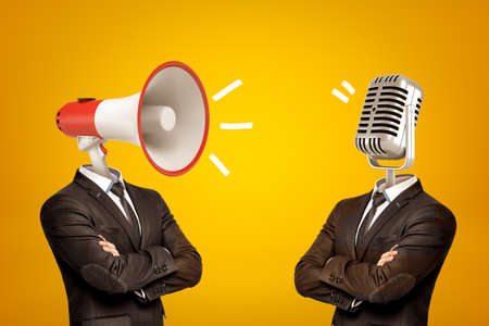 Waist-deep view of two businessmen standing in half-turn, arms folded, with megaphone and microphone...