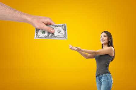 Side crop view of young pretty girl in casual clothes holding out hands to take money from big mans...