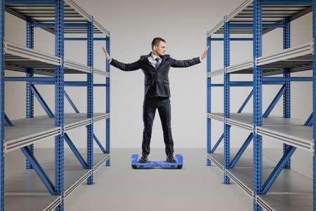 A businessman stands on a self-balancing scooter between two storage racks.の写真素材