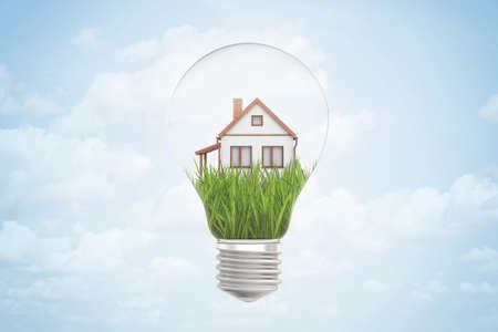 3d rendering of lightbulb in air, with green grass and small house inside, against blue sky with clouds.の写真素材