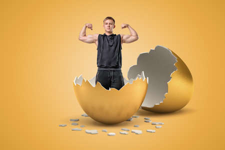 Young fit man raising hands and showing his muscles who has just hatched out from golden egg.
