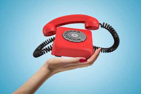 Side closeup of womans hand facing up and holding ringing retro phone on light blue background.
