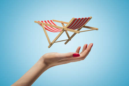 Side closeup of womans hand facing up and levitating small striped chaise-longue on light blue...