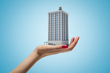 Female hand holding high building on blue backgroundの写真素材