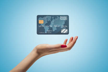 Side closeup of womans hand facing up and levitating plastic bank card on light blue gradient background.の写真素材