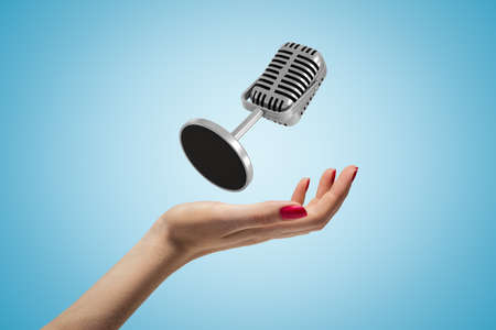 Side closeup of woman hand facing up and levitating microphone on light blue gradient background.の写真素材