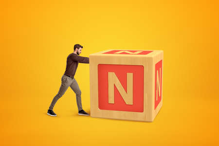 Man wearing casual clothes pushing big alphabet toy block on yellow background.の写真素材
