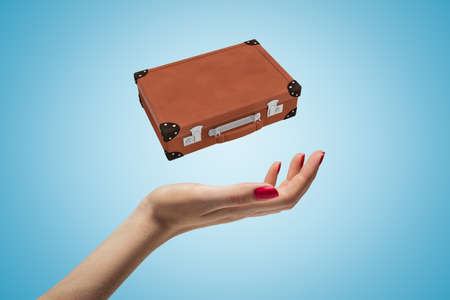 Closeup of woman's hand levitating brown travel case on light blue background.の写真素材